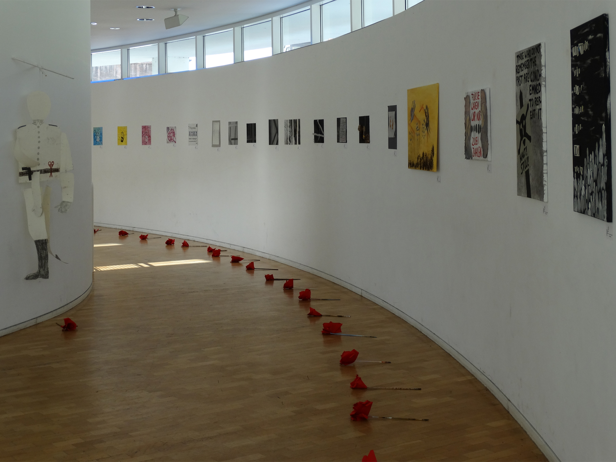 Die Ausstellung im Saal-Foyer des Stadthauses. Vor den Bildern liegen rote Rosen aus Krepppapier