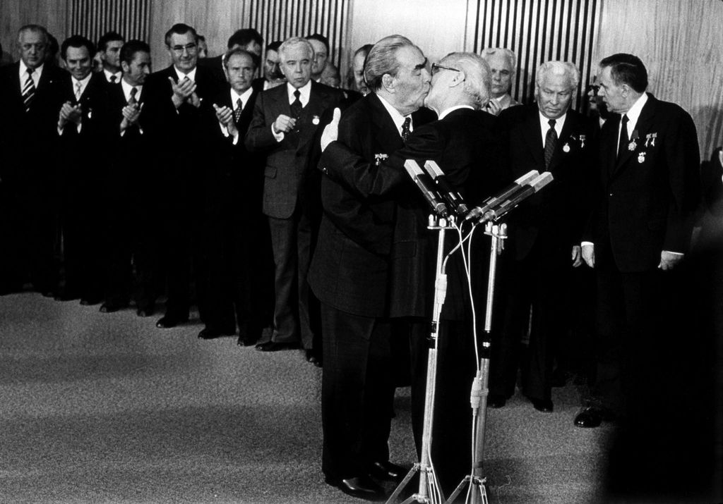 Schwarz-weiße Fotografie. Im Vordergrund hinter einem Mirkofonständer Leonid Breschnew und Erich Honecker beim "Bruderkuss", im Hintergrund zahlreiche applaudierende, dunkel gekleidete Herren. Das Bild entstand am 30. Jahrestag der DDR (7. Oktober 1979). Foto: Barbara Klemm