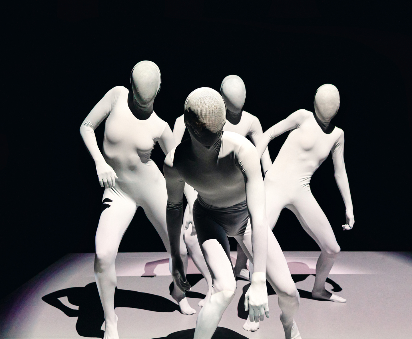 Vier komplett verhüllte Tänzer*innen vor dunklem Grund 
