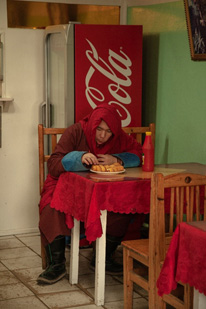Mönch sitzt vor Coca-Cola-Kühlschrank und isst Fastfood
