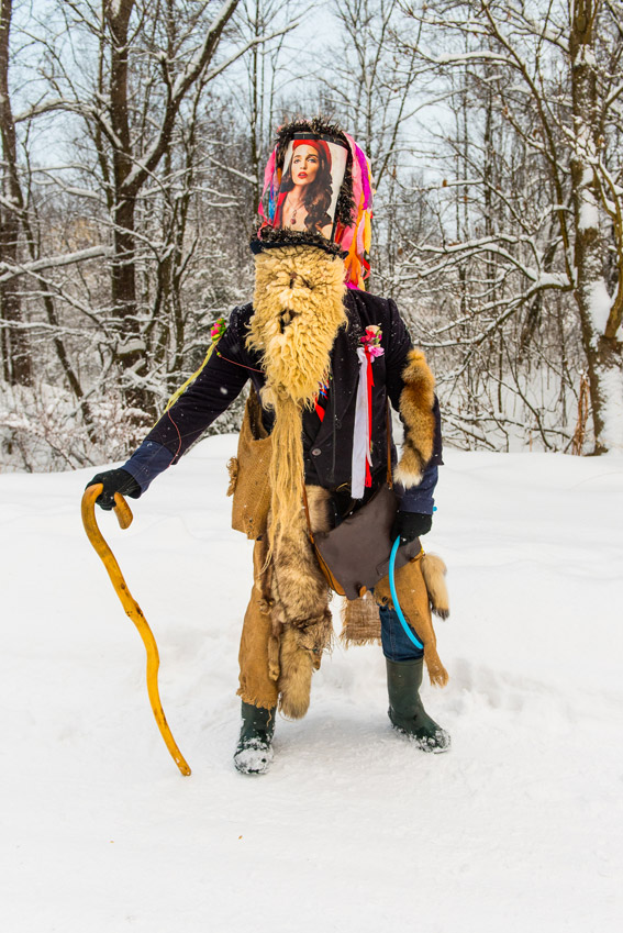 Ein maskierter und verkleideter Mensch steht mit einem Stock im Schnee
