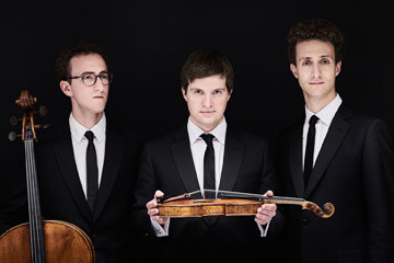 Drei Musiker in schwarzen Anzügen und Krawatte, zwei davon mit Instrumenten
